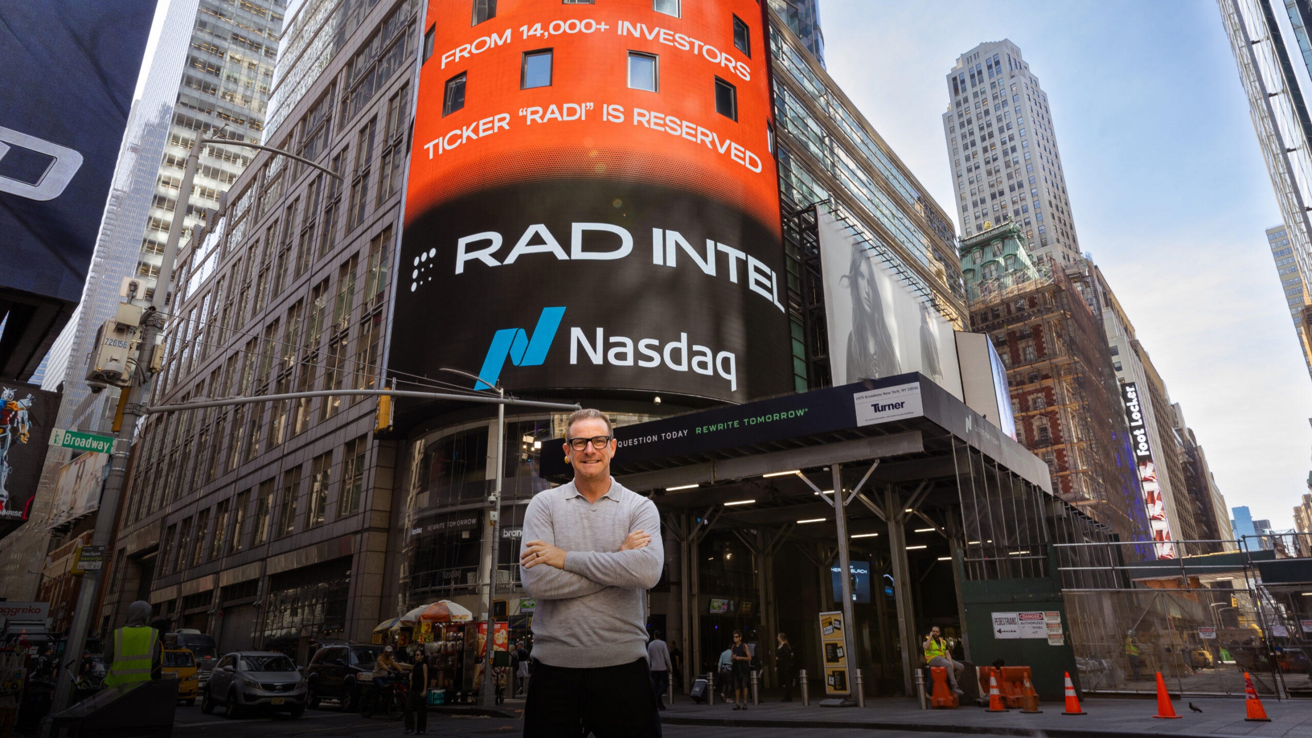 RAD Intel CEO standing in front of NASDAQ building in Times Square, with RAD INTEL featured on the Nasdaq billboard
